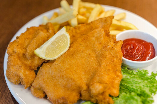 Knusprig gebackenes Schnitzel mit Pommes, Zitrone und Sauce auf einem Teller serviert