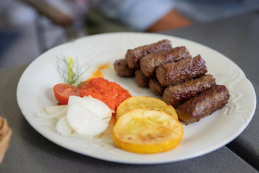 Gegrillte Cevapcici mit Ajvar, Zwiebeln und Beilage auf einem Teller serviert